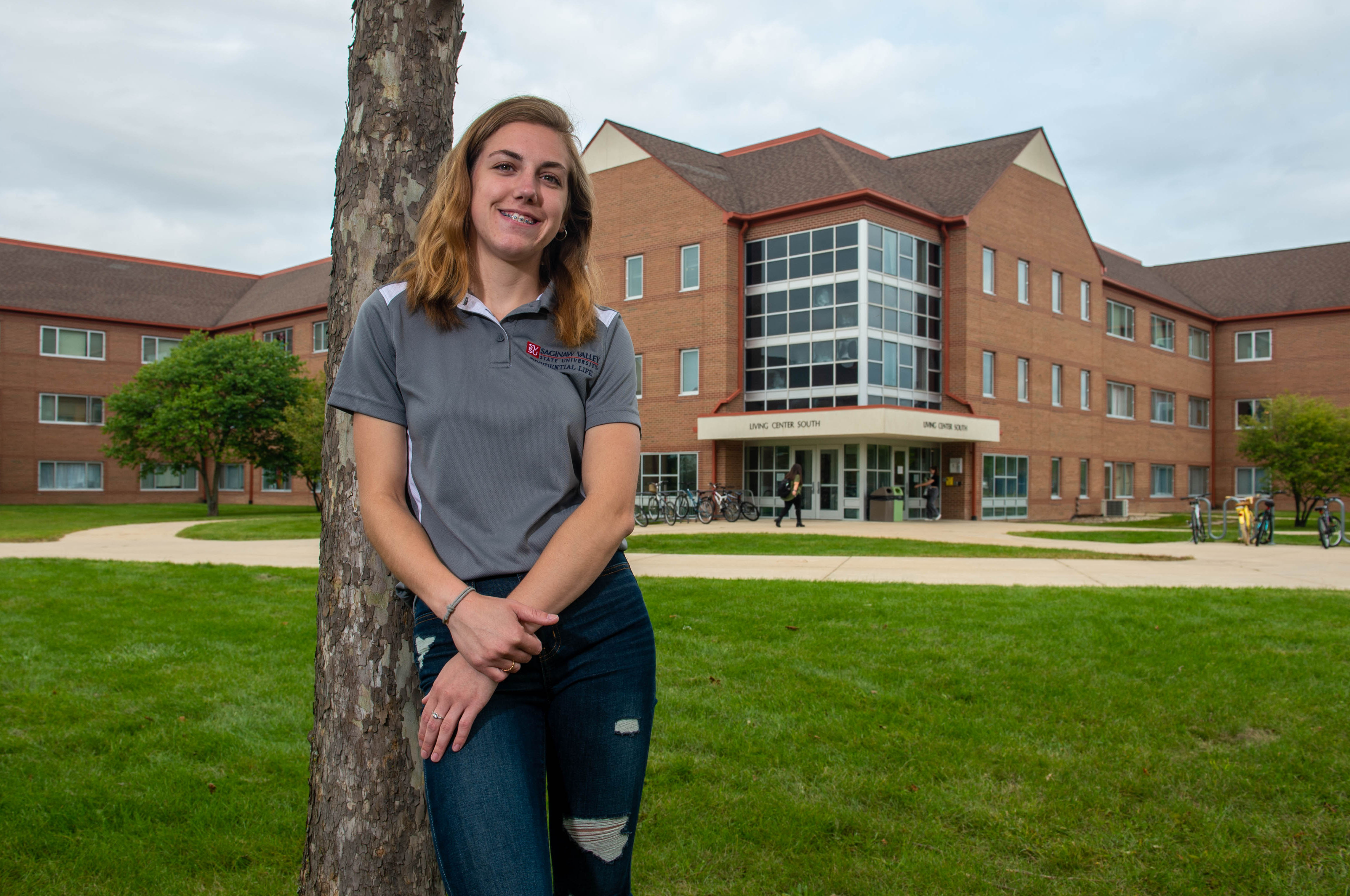 Young woman leaning on tree in front of dorms